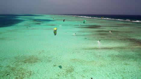 Kitesurfistas-En-El-Arrecife-De-Coral-Los-Roques,-Vibrantes-Aguas-Color-Turquesa-Bajo-Un-Cielo-Despejado,-Vista-Aérea