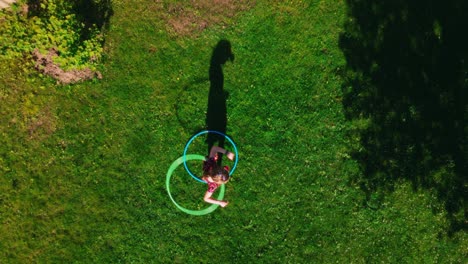 Top-aerial-view-on-girl-hoola-hooping-with-long-shadow-on-summer-grass-field-with-long-shadow