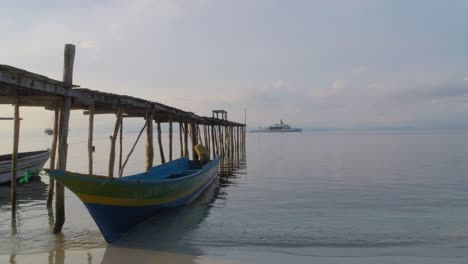 A-traditional-boat-docked-by-a-rustic-wooden-pier-on-Kri-Island-in-the-Raja-Ampat-Archipelago,-Indonesia