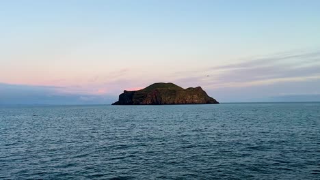 Remote-island-in-Vestmannaeyjar,-Iceland,-under-soft-sunset-hues,-tranquil-sea-foreground