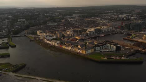 Antena-De-La-Icónica-Galway,-La-Larga-Caminata,-El-Puerto-Y-El-Río-Corrib-En-La-Luz-Dorada-Del-Atardecer.