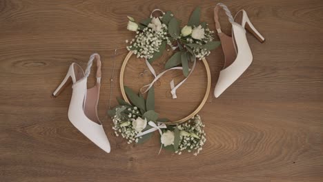 White-high-heeled-shoes-with-floral-wreath-and-jewelry-on-a-wooden-floor