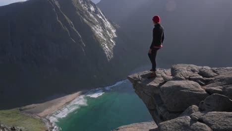 Pan-of-a-woman-hiking-the-Peak-of-the-Kvalvika-Beach-hike-on-a-beautiful-sunny-day-in-the-Lofoten-Islands,-Norway