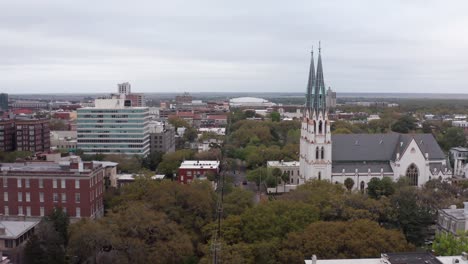 Low-aerial-shot-flying-over-the-famous-city-squares-of-Savannah,-Georgia-towards-the-Cathedral-Basilica-of-Saint-John-the-Baptist