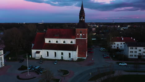 Drone-rises-along-Latvia-streets-to-church-with-spire-bell-tower-overlooking-town