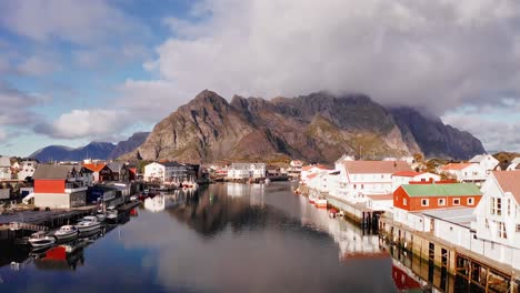 Flying-low-in-the-port-of-Henningsvær-then-revealing-the-mountains-in-the-background-on-a-beautiful-day-in-the-Lofoten-Islands,-Norway