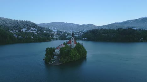 Vista-Aérea-De-Una-Pequeña-Isla-Verde-Con-La-Iglesia-De-La-Asunción-En-Medio-Del-Tranquilo-Lago-Bled,-Eslovenia