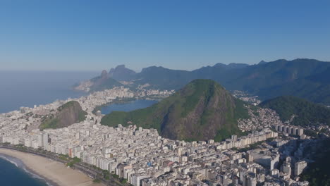 Wide,-aerial-footage-rotating-around-Stone-Maroca-with-apartment,-buildings-and-beaches-in-the-foreground-in-Rio-de-Janeiro