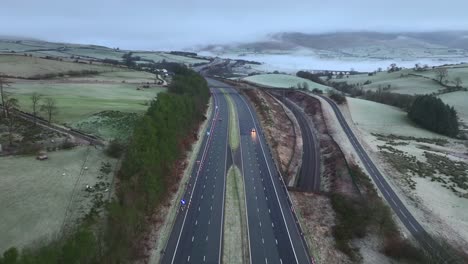 Flying-down-the-centre-of-M6-highway-with-light-traffic-at-dawn-in-winter-with-background-hills-covered-in-mist,-fog-and-low-cloud