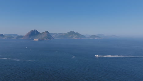 Imágenes-Aéreas-Del-Farol-Da-Fortaleza-De-Santa-Cruz-Frente-A-La-Costa-De-Río-De-Janeiro-Con-Un-Velero-Cruzando-Las-Aguas-Frente-A-él