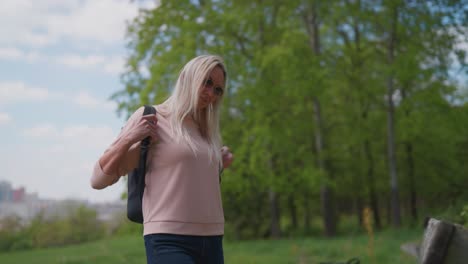 Woman-walk-at-green-suburb-area-and-put-backpack-on-wooden-park-bench