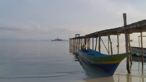 Small-wooden-boat-anchored-in-Raja-Ampat-at-jetty-with-luxury-superyacht-Wanderlust-in-background