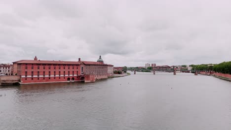 Serene-riverside-view-of-historic-brick-building-with-dome-and-bridge-in-Toulouse,-France