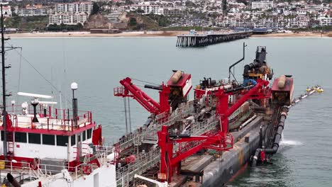 Un-Buque-De-Dragado-Trabaja-En-El-Proyecto-De-Reemplazo-De-Arena-De-San-Clemente-Con-Un-Muelle-Y-La-Ciudad-Al-Fondo