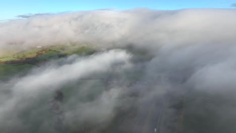 Flying-above-thick-mist-with-pan-up-revealing-thick-cloud-bank-covering-large-hill
