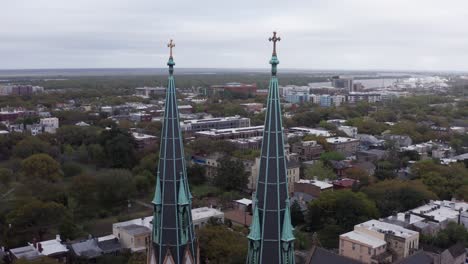 Toma-Panorámica-Aérea-De-Paralaje-De-Las-Agujas-Góticas-En-Lo-Alto-De-La-Basílica-Catedral-De-San-Juan-Bautista-En-Savannah,-Georgia