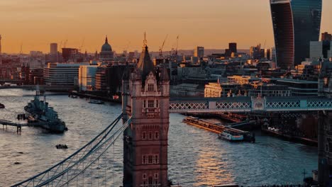 Drohnenaufnahme-Der-Tower-Bridge-Bei-Sonnenuntergang-Mit-Booten-Auf-Der-Themse-Und-Walkie-Talkie-Gebäude-Im-Hintergrund