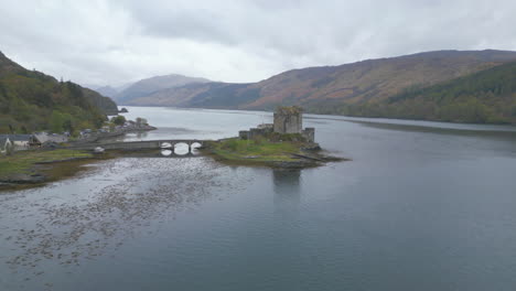 Eilean-donan-castle-and-surrounding-scottish-highlands-on-a-cloudy-day,-aerial-view