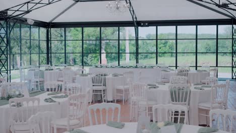 Elegantes-Hochzeitsempfangs-Setup-Mit-Weißen-Tischen-Und-Stühlen-In-Einem-Veranstaltungsort-Mit-Glaswänden