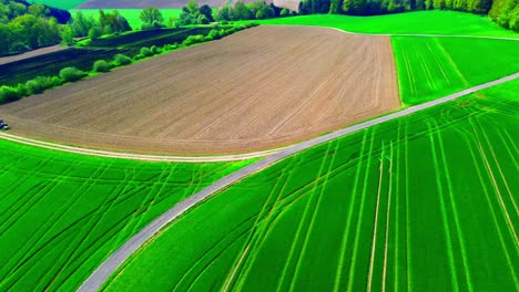 Vista-Aérea-De-Tierras-De-Cultivo-Verdes-Y-Marrones-Con-Tractor-En-Carretera-Curva