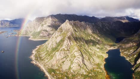 Dreamy-aerial-orbit-around-the-Lofthaugen-mountains,-with-an-amazing-rainbow-in-the-background,-near-Henningsvær,-Lofoten-Islands,-Norway