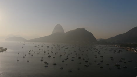 Aerial-footage-flying-over-anchored-boats-in-the-Botafogo-bay-in-the-hazy-light-of-sunrise-with-Sugarloaf-mountain-in-the-background