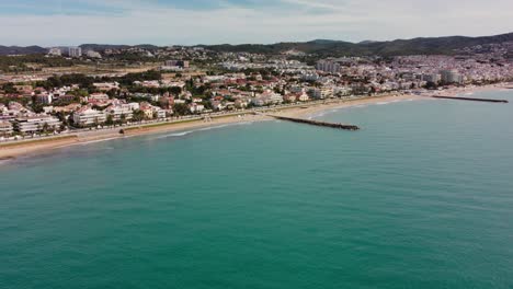 Sitges,-España,-Mostrando-La-Costa-Y-El-Paisaje-Urbano-Con-Montañas-Al-Fondo,-Vista-Aérea