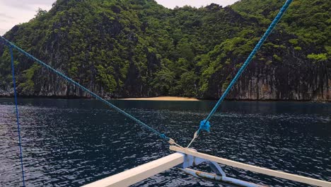 Filipino-Bangka-Catamaran-Boat-Sailing-by-Hidden-Beach-Under-Limestone-Cliffs-on-Uninhabited-Island,-Passenger-POV