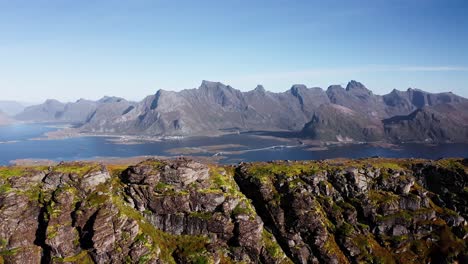 Luftaufnahme-Einer-Klippe-In-Der-Nähe-Des-Strandes-Von-Kvalvika-Mit-Wunderschönen-Bergen-Und-Einem-Klaren-Blauen-Himmel-Im-Hintergrund,-Lofoten-Inseln,-Norwegen