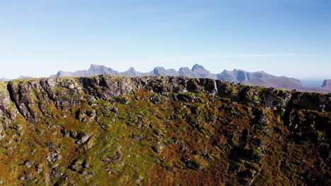 Reveal-of-a-gorgeous-chain-of-mountains-behind-a-majestic-cliff-on-a-blue-bird-clear-sky-day-in-the,-near-Kvalvika-beach,-Lofoten-Islands,-Norway