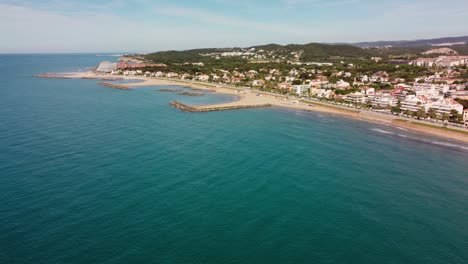 Sitges'-coastline-with-sandy-beaches-and-vibrant-town-during-a-sunny-day,-aerial-view