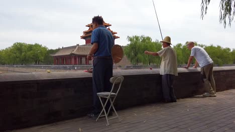 Three-chinese-fishers-do-fishing-on-the-corner-of-the-perimetral-channel-of-the-forbidden-city,-Beijing,-China