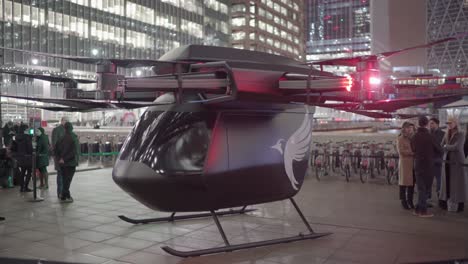 Futuristisches-Echtes-Drohnentaxi-Am-Canary-Wharf-Square-In-London-Mit-Eingeschaltetem-Licht-Und-Neugierigen-Menschen-Um-Es-Herum