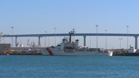 US-Coastguard-Alert-WMEC-630-medium-endurance-cutter-ship-anchored-at-the-port-with-the-Coronado-bridge-in-the-background,-locked-establishing-shot