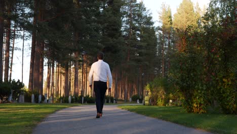 Man-walking-towards-gravestones-in-a-garden-cemetery-in-Sweden-on-a-sunny-afternoon