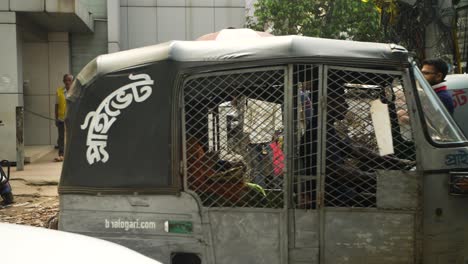 Busy-street-of-Dhaka,-rickshaws-passing-by-market-stalls