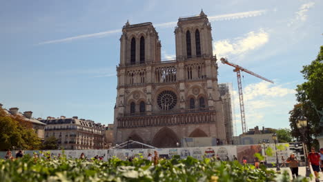 Tourists-walking-past-the-Notre-Dame-Cathedral-in-Paris,-France-near-the-River-Seine-under-construction-after-fire-damage