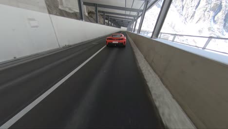 High-speed-chase-following-a-ferrari-driving-through-a-mountain-pass-tunnel-with-snow-covered-areas-visible-in-the-distance