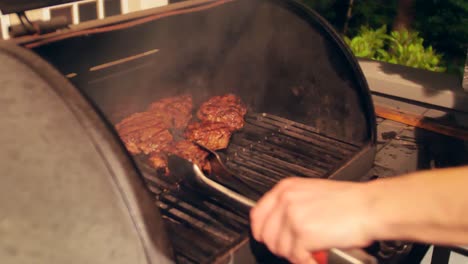 Kaukasische-Männliche-Hand-Bewegt-Dicke,-Saftige-Steaks,-Die-Auf-Einem-Außengrill-Im-Hinterhof-Kochen-Und-Rauchen,-Nahaufnahme-Der-Pfanne