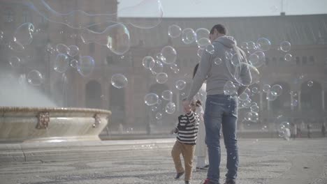 Excited-little-girl-pops-soap-bubbles-next-to-her-dad-in-La-Plaza-de-España,-Sevilla-Spain