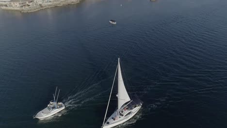 Toma-Aérea-De-Un-Velero-Blanco-Y-Un-Barco-Pesquero-Que-Se-Dirige-A-La-Bahía-De-Newport-En-Newport-Beach,-California,-Con-Pirates-Cove-Al-Fondo