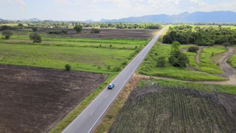 An-Aerial-Drone-Shot-of-a-Blue-Toyota-CHR-Vehicle-Driving-Along-a-Straight-Road-in-the-Countryside-of-Lopburi,-Thailand