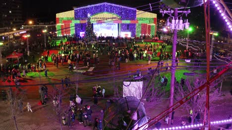 Aerial-ascending-shot-of-a-ferris-wheel-with-Fort-Lee-Tree-Lighting-ceremony-in-the-background,-New-Jersey