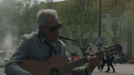Elderly-man-soulfully-playing-the-guitar-in-downtown-Stuttgart-square-at-noon,-Germany,-Europe,-panning-view-angle