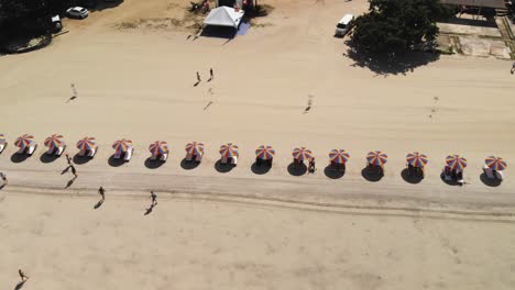 Slow-motion-top-down-shot-of-tourists-at-the-beach-with-colorful-beach-umbrellas