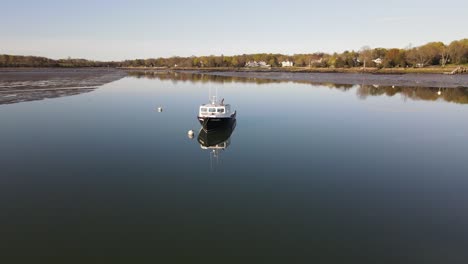 A-drone-flies-over-vacant-moorings-and-a-solo-fishing-vessel-at-dusk-on-a-mirror-smooth-Hingham-Harbor
