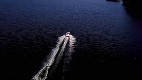 Girl-Water-Skis-Away-on-Blue-Lake,-Wide-Aerial-Drone-Tracking-Overhead