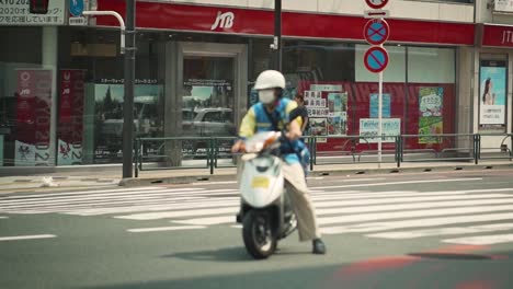 Maskierter-Motorradfahrer-Rückt-In-Zeitlupe-In-Den-Fokus,-Während-Er-Auf-Seinem-Weg-Zur-Arbeit-An-Einer-Ampel-An-Einer-Kreuzung-In-Tokio,-Japan-Wartet