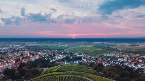 Vista-Real-De-Drones-Sobre-Viñedos-Con-Un-Pequeño-Pueblo-Europeo,-Una-Cambiante-Puesta-De-Sol-Púrpura