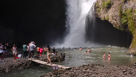 Mujer-Asiática-Disfrutando-De-La-Famosa-Cascada-De-Tegenungan-En-Bali-Con-Gente-Bañándose-En-Ella-En-Segundo-Plano.